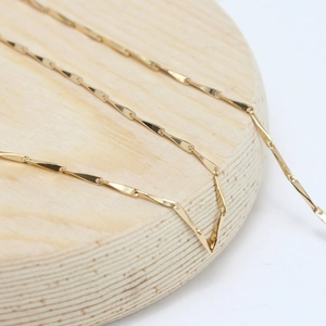 Macro detail of 14K gold plated flat twist chain links on a wooden display stand