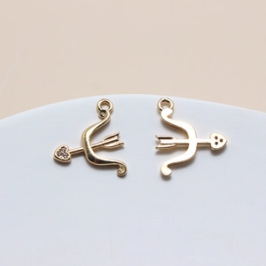 Close-up of golden bow and arrow pendants with heart details and cubic zirconia for DIY jewelry