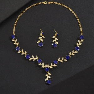 Dettaglio della collana floreale dorata e orecchini con cristalli blu e petali bianchi