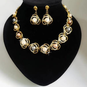 Detail van een gouden sieradenset met parels en fonkelende witte strass-steentjes op zwart