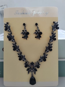 Dettaglio di un set di collana e orecchini vintage con cristalli neri e motivi floreali