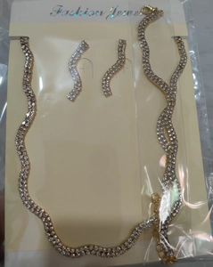 Détail du collier et des boucles d'oreilles dorés ondulés avec des strass brillants