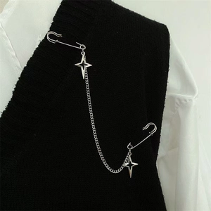 Détail d'une broche à chaîne argentée avec étoiles fixée sur une tenue noir et blanc