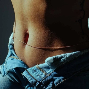 Gros plan d'une fine chaîne de taille perlée en or rose portée par un mannequin femme