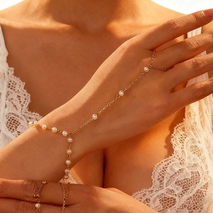 Detail eines Goldketten-Fingerarmbands mit weißen Perlen an einem Handmodell