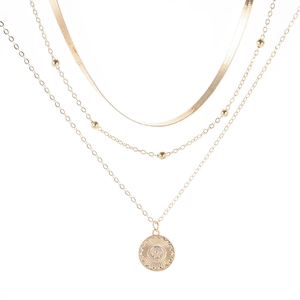 Detail of layered gold necklace featuring snake chain and sun medallion pendant