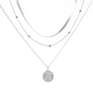 Detailed close-up of a silver triple-layered necklace featuring a sunburst pendant and snake chain