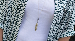 Detalle de collar con colgante de pluma vintage y cuentas negras en una modelo con camisa