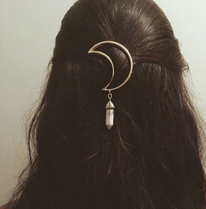 Detail view of a gold crescent moon hair clip with a white hexagonal stone pendant on hair