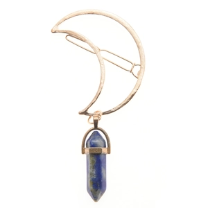 Detail of a golden crescent moon hair clip with a blue hexagonal crystal pendant charm