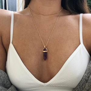 Double-layered gold necklace featuring a purple hexagonal crystal column pendant on model