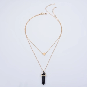 Detail of double-layer gold necklace featuring a heart charm and black hexagonal prism pendant
