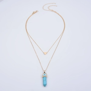 Detail of layered gold necklace featuring a heart pendant and blue hexagonal crystal