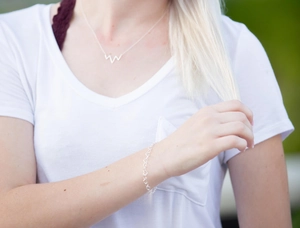 Detail of silver heart link bracelet and geometric necklace worn by model outdoors