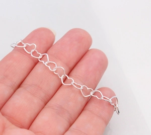 Detailed shot of a silver hollow heart link bracelet held in hand with glossy finish