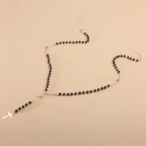 Lange kralenketting met zwarte harskralen en een gouden kruisvormige kwastjes hanger