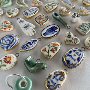 Detail of ceramic charms with gold edges featuring colorful painted patterns and metallic loops