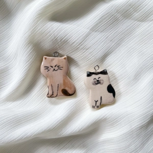 Hand-painted ceramic cat pendants in orange and black-white with metal hanging loops