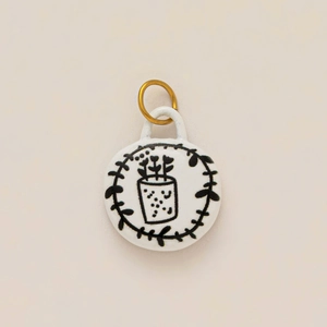 Detail of round ceramic pendant with hand-drawn botanical illustration and gold plated ring
