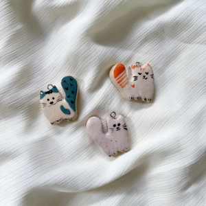 Three hand-painted ceramic cat pendants with stainless steel loops on white fabric