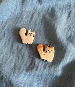 Detail of two hand-painted ceramic cat pendants on blue textured fabric background