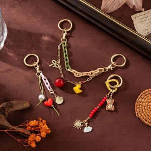 Three DIY fashion bag charms with colorful heart, duck, and bear pendants on dark background