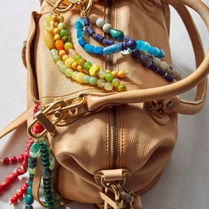 Colorful gemstone beaded charm with gold metal clasp on a leather handbag accessory