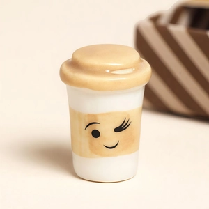 Süße cremefarbene Kaffeetassen-Miniatur mit zwinkerndem Gesicht und braunem Streifen