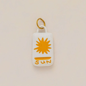 Detailed macro view of white ceramic sun pendant with golden metal loop and engraving