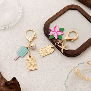 Detail of summer charms with enamel ice cream, pink flower, and starfish on gold keychains