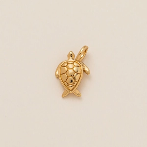Détail d'un pendentif tortue dorée avec finition polie et texture de carapace en nid d'abeille
