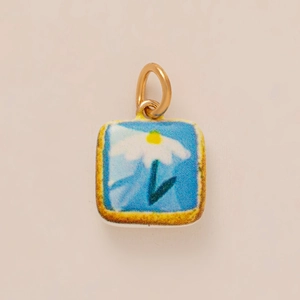Macro shot of square light blue enamel daisy charm with a polished gold ring attachment