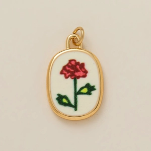 Vue détaillée d'un pendentif ovale doré avec broderie de rose rouge sur fond blanc
