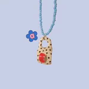 Close-up of beaded necklace featuring a ceramic strawberry handbag pendant on purple background