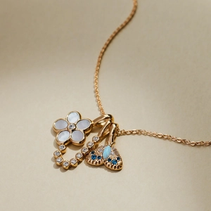 Close-up of gold necklace featuring shell flower, diamond bar, and blue gemstone charms