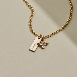 Detail of gold beehive pendant and rectangular tag engraved with 2002 on a vintage chain