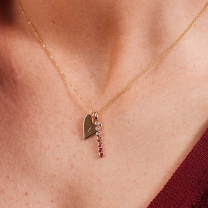 Close-up of gold chain necklace with letter L heart and gradient pink gem heart pendants