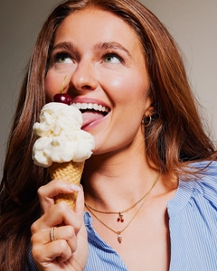 Close-up of model wearing gold cherry and ice cream pendants with elegant rings
