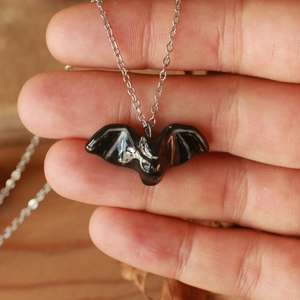 Dettaglio di un piccolo ciondolo a pipistrello nero lucido su una catena d'argento