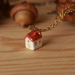 Dettaglio di un ciondolo a forma di casa con tetto rosso e punti dorati su legno chiaro