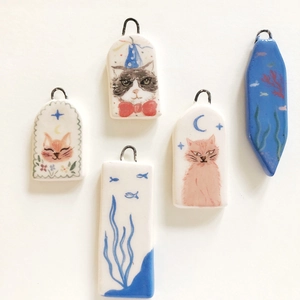 Dettaglio macro di cinque ciondoli in ceramica colorata con gatti e motivi marini