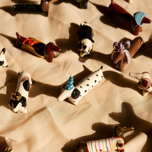 Detailaufnahme von bunten Keramik-Dackel-Anhängern auf beige gefalteten Seidenstoff