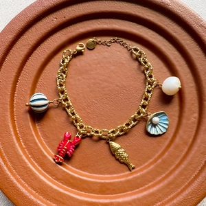 Détail d'un bracelet doré avec breloques émaillées de homard, poisson et coquillage sur plateau