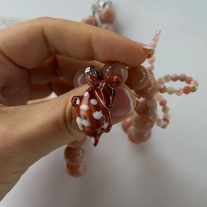 Close-up of cute deer pendant on pink semi-transparent beaded necklace held in hand
