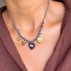 Détail d'un collier en cordon bleu avec œil protecteur doré et breloques de cœur