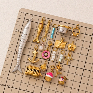 18K gold plated stainless steel fish pendants and assorted charms on a grid background