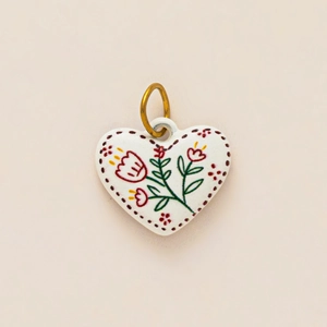 Detailed view of heart-shaped ceramic pendant with hand-painted floral patterns and metal ring