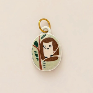 Detailed view of an oval ceramic owl pendant with a 18K gold-plated stainless steel loop