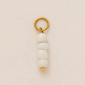 Vertical detail of 18K gold-plated metal ring with four white ceramic beads on light surface