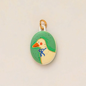 Detail of an oval white pendant featuring a cute goose illustration with a gold hanging loop